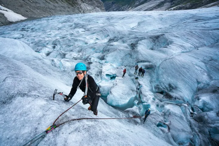 Actual operator tour-page photo, alt text: “Person in blue helmet climbing a glacier, with others in background on icy terrain.”